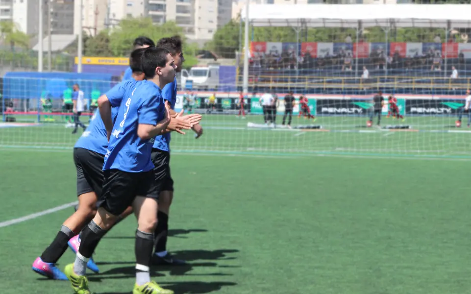 Jogadores comemorando em campo durante uma partida de futebol escolar